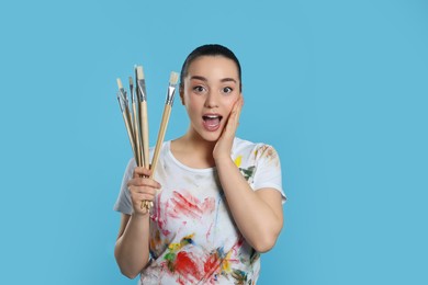Photo of Woman with paintbrushes on light blue background. Young artist