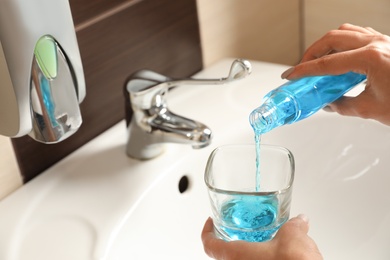Photo of Woman pouring mouthwash from bottle into glass in bathroom, closeup. Teeth care