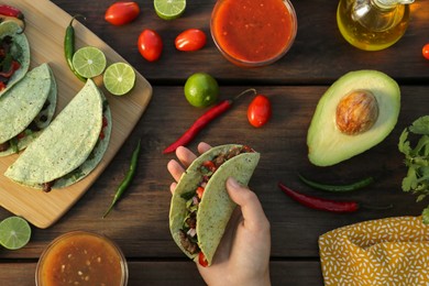 Photo of Woman holding delicious taco at wooden table, top view. Mexican food