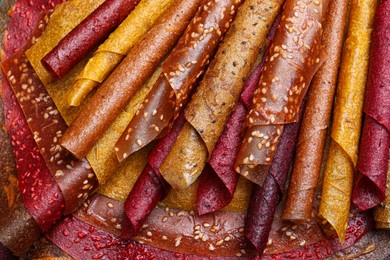 Delicious fruit leather rolls as background, top view