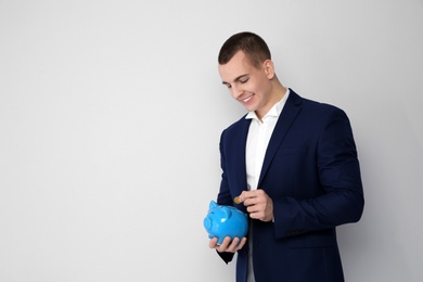 Photo of Young businessman putting coin into piggy bank on white background. Space for text