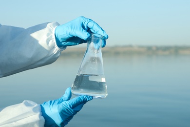 Photo of Scientist with conical flask taking sample from river for analysis, closeup