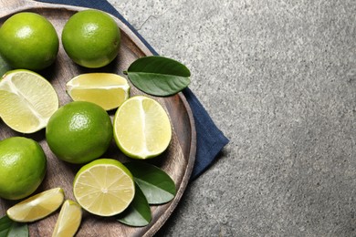 Photo of Fresh ripe limes and leaves on grey table, top view. Space for text