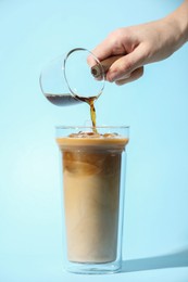 Photo of Woman making iced coffee on light blue background, closeup