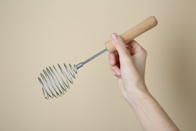 Photo of Woman holding metal whisk on beige background, closeup