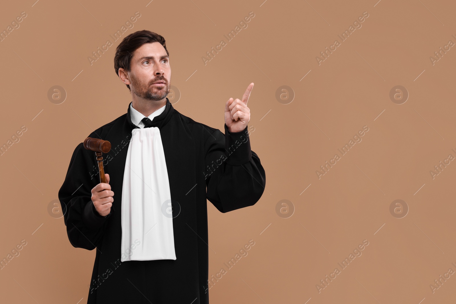 Photo of Judge with gavel pointing at something on light brown background. Space for text