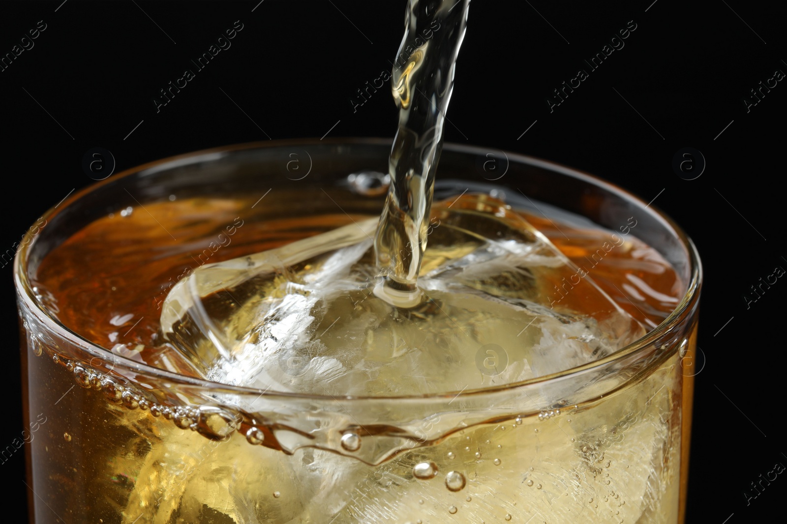 Photo of Pouring tasty whiskey into glass with ice on black background, closeup