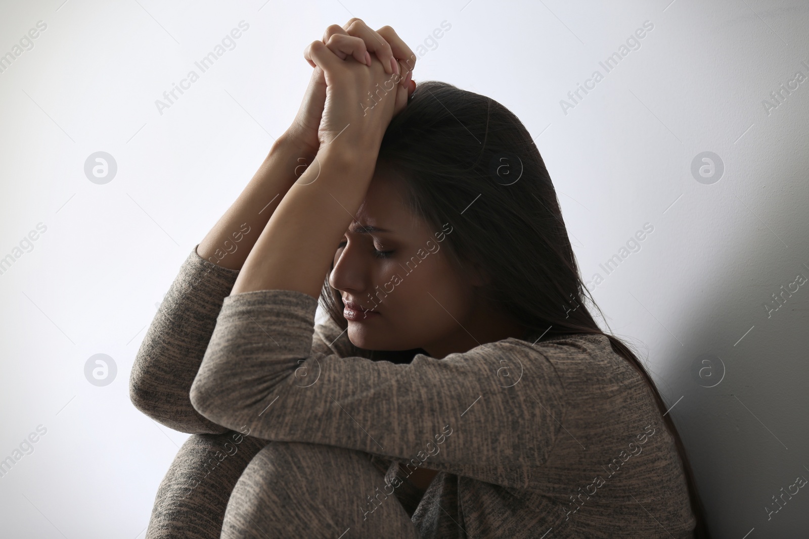 Photo of Depressed young woman sitting near light wall