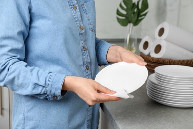 Photo of Woman wiping ceramic plate with paper towel indoors, closeup