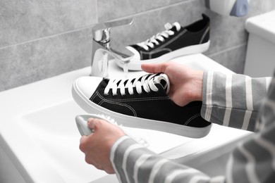 Photo of Woman washing stylish sneakers with brush in sink, closeup