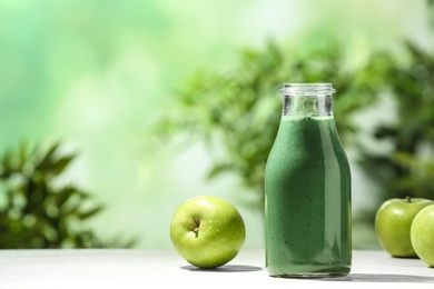 Bottle of spirulina smoothie and apples on table against blurred background. Space for text