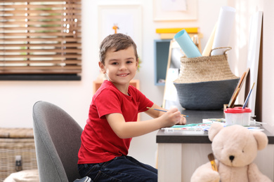 Little child painting at table in room