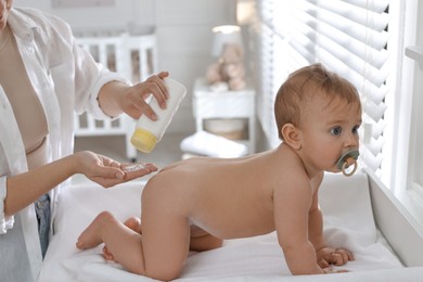 Mother applying dusting powder on her cute baby at home, closeup