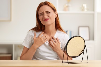 Photo of Suffering from allergy. Young woman looking in mirror and scratching her neck at home