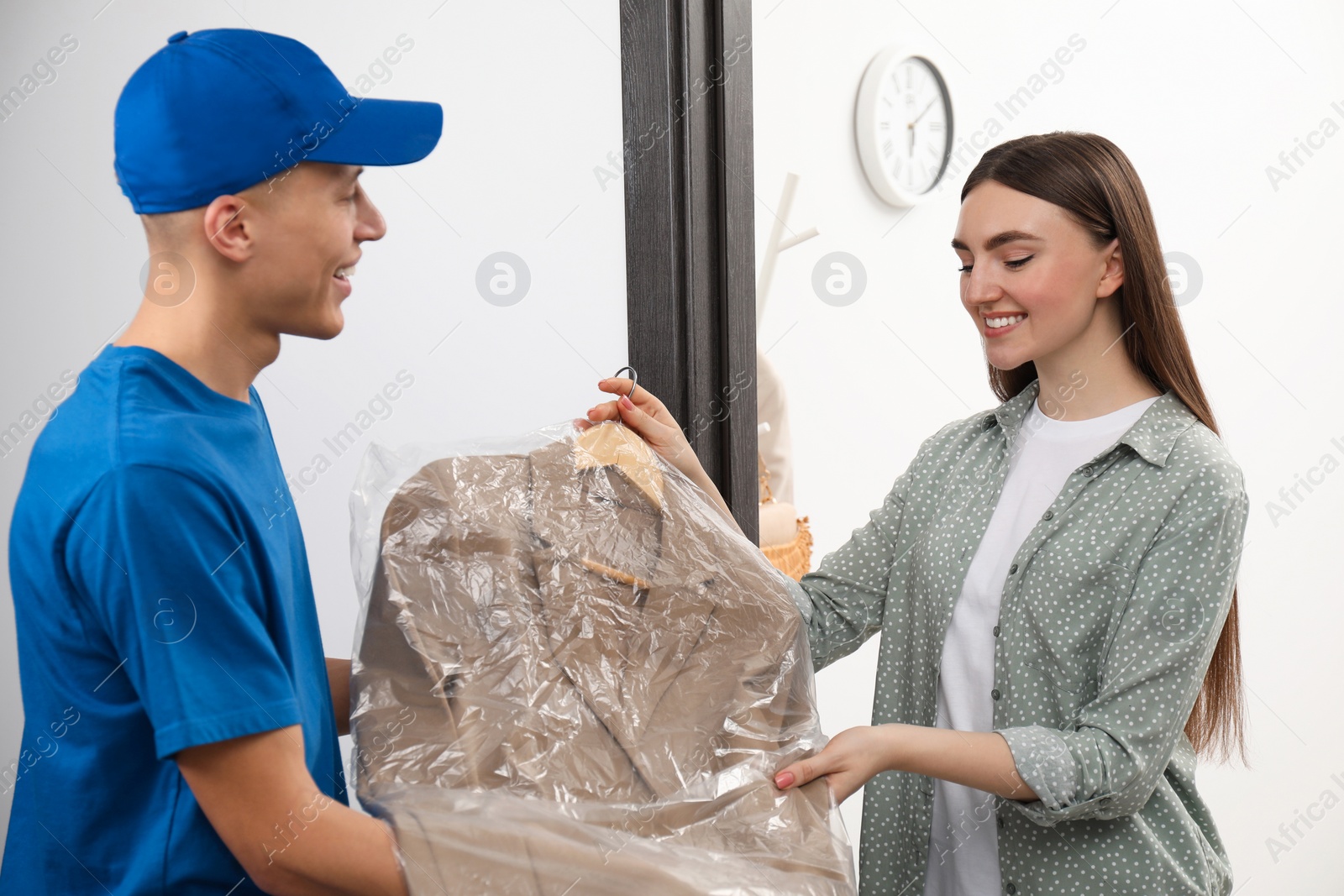 Photo of Dry-cleaning delivery. Courier giving jacket in plastic bag to woman indoors