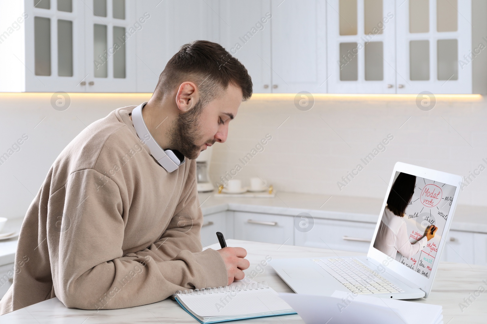 Image of Young man with modern laptop at online lesson in kitchen. E-learning