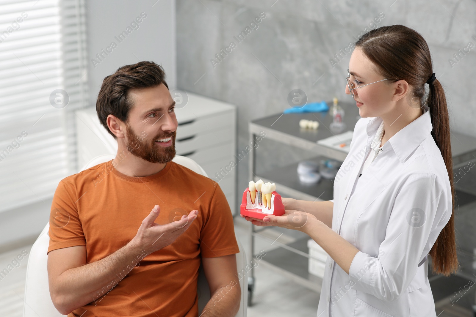 Photo of Doctor with educational model of dental implant consulting patient in clinic