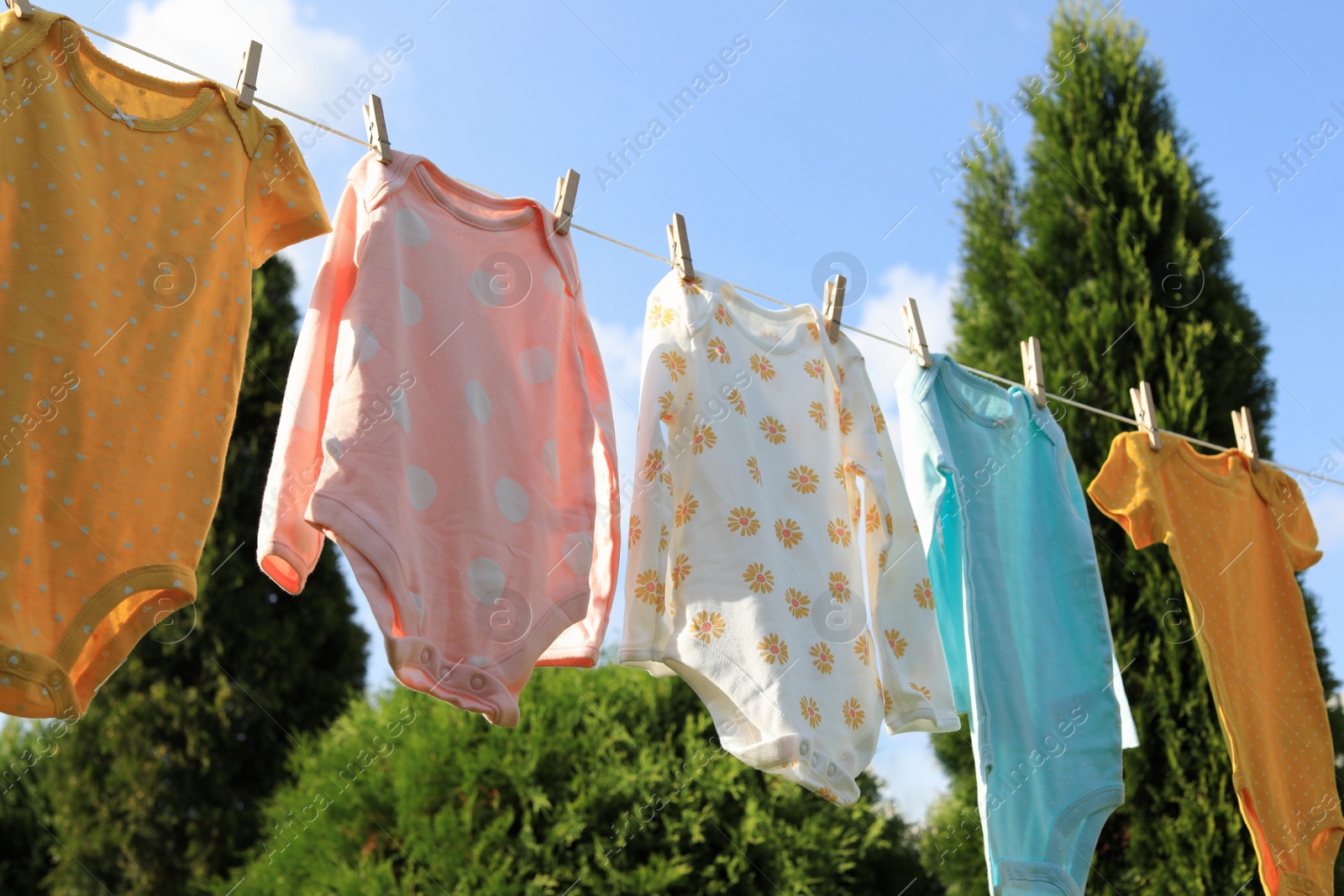 Photo of Clean baby onesies hanging on washing line in garden. Drying clothes