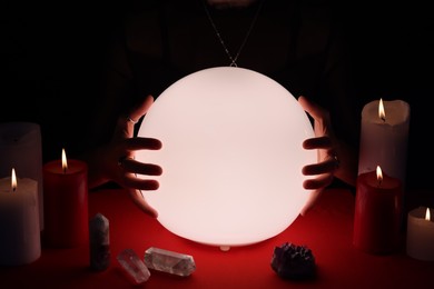 Photo of Soothsayer using glowing crystal ball to predict future  at table in darkness, closeup. Fortune telling