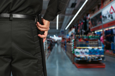 Image of Security guard in uniform with police baton in shopping mall, closeup. Space for text