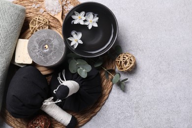 Flat lay composition with herbal massage bags, spa products and flowers on light grey table. Space for text