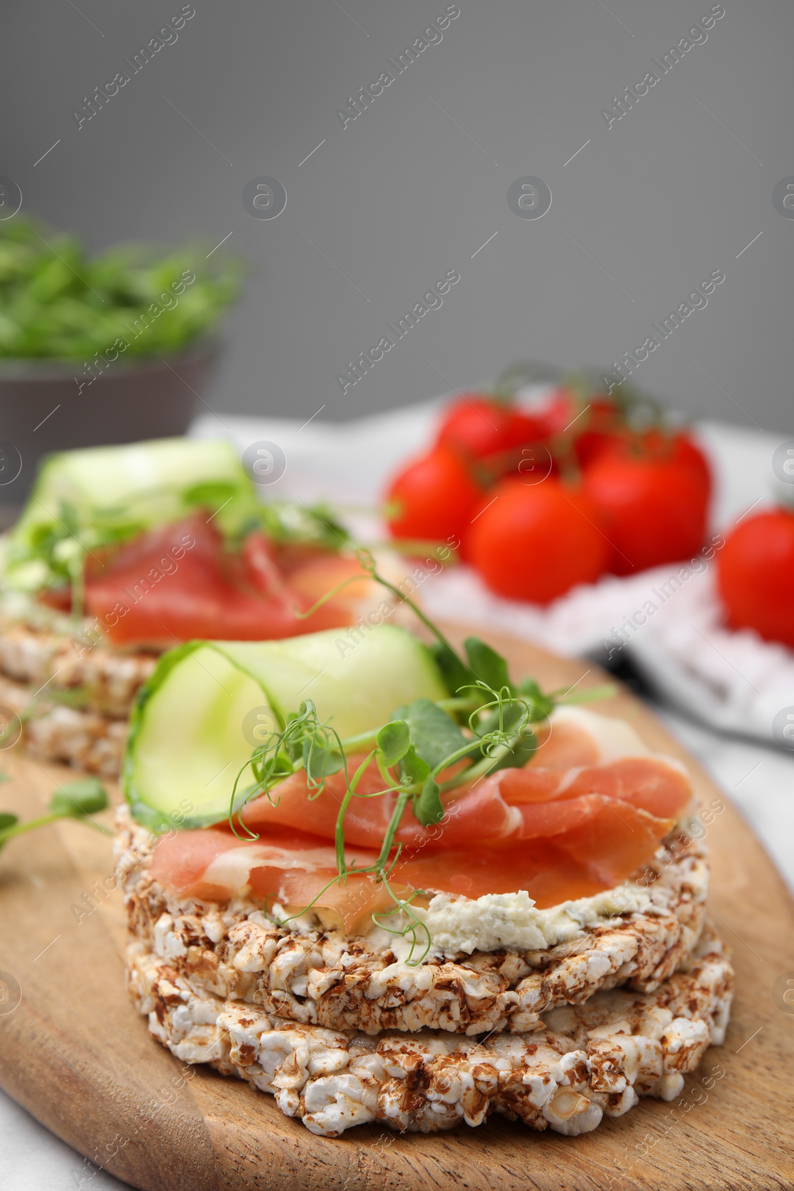 Photo of Crunchy buckwheat cakes with cream cheese, prosciutto and cucumber slices on wooden board, closeup