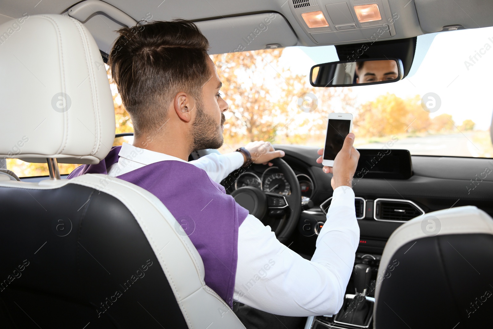 Photo of Young man using phone in driver's seat of modern car