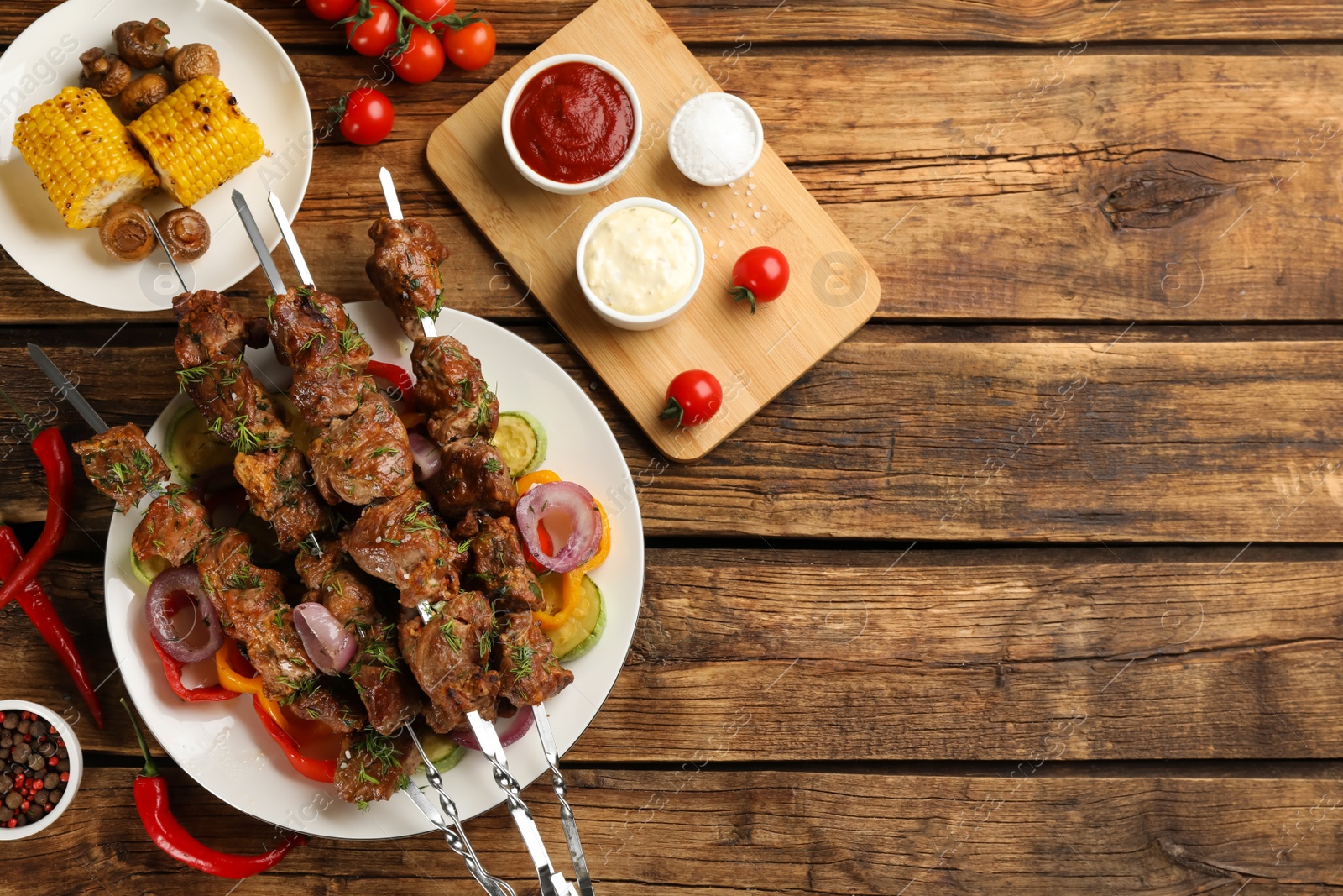 Photo of Metal skewers with delicious meat, sauces and vegetables served on wooden table, flat lay. Space for text