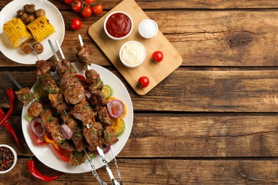 Photo of Metal skewers with delicious meat, sauces and vegetables served on wooden table, flat lay. Space for text