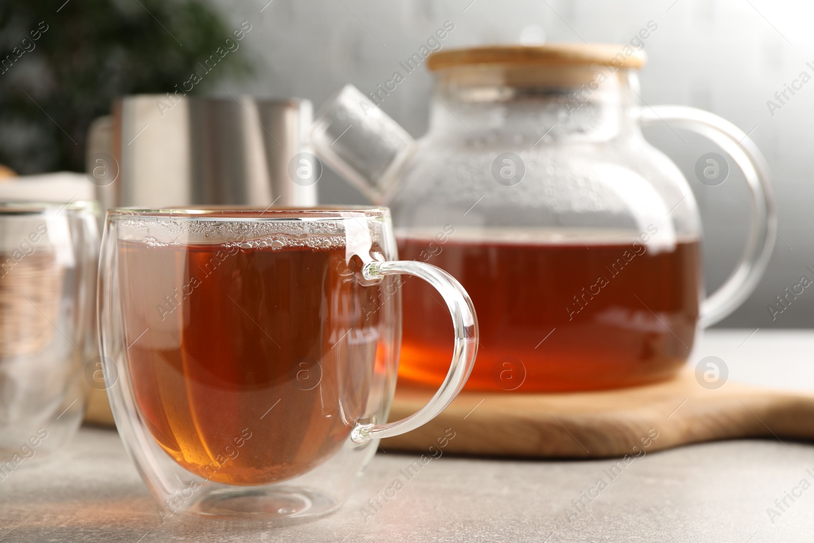 Photo of Aromatic tea in glass cup and teapot on light grey table