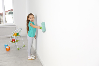 Little child painting with roller brush on white wall indoors. Space for text