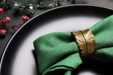 Photo of Plate with green fabric napkin and decorative ring on black background, closeup