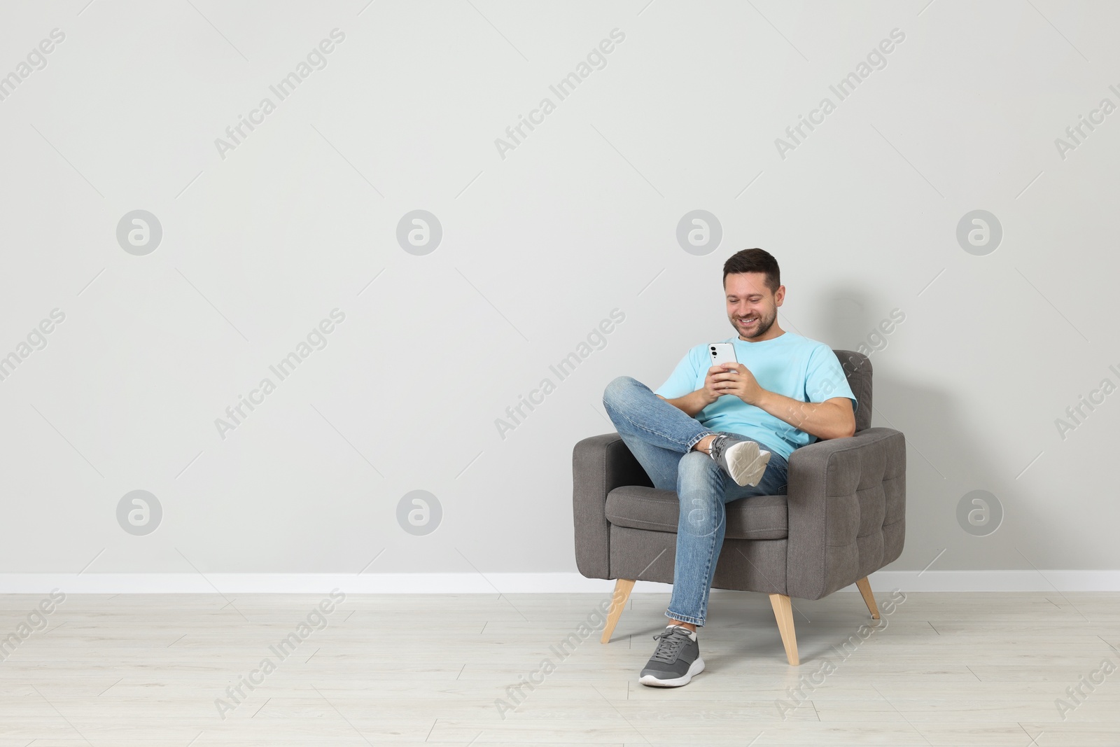 Photo of Happy man sitting in armchair and using smartphone indoors, space for text