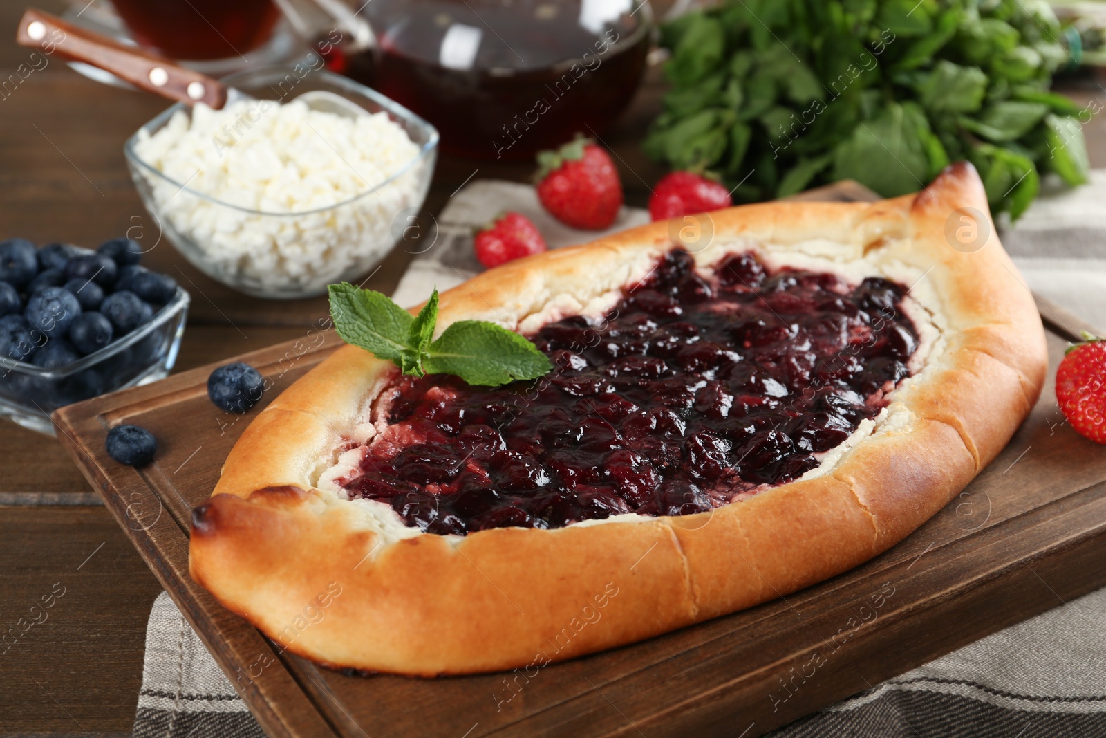 Photo of Delicious sweet cottage cheese pastry with cherry jam and fresh berries on wooden table, closeup