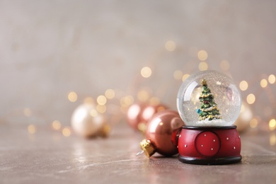 Photo of Snow globe with Christmas tree and decorations on marble table against festive lights, space for text
