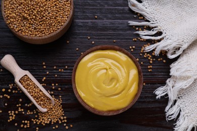 Delicious mustard and seeds on dark wooden table, flat lay