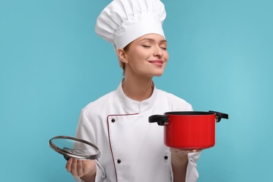 Photo of Happy woman chef in uniform holding cooking pot on light blue background