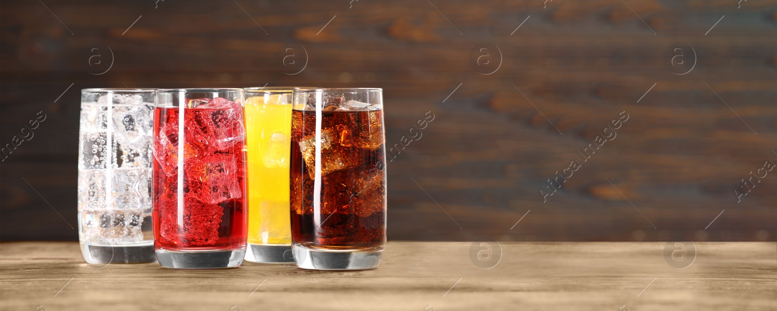 Image of Tasty refreshing soda drinks with ice cubes on wooden table. Banner design with space for text