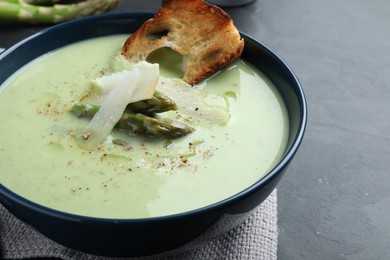 Photo of Bowl of delicious asparagus soup served on dark table, closeup