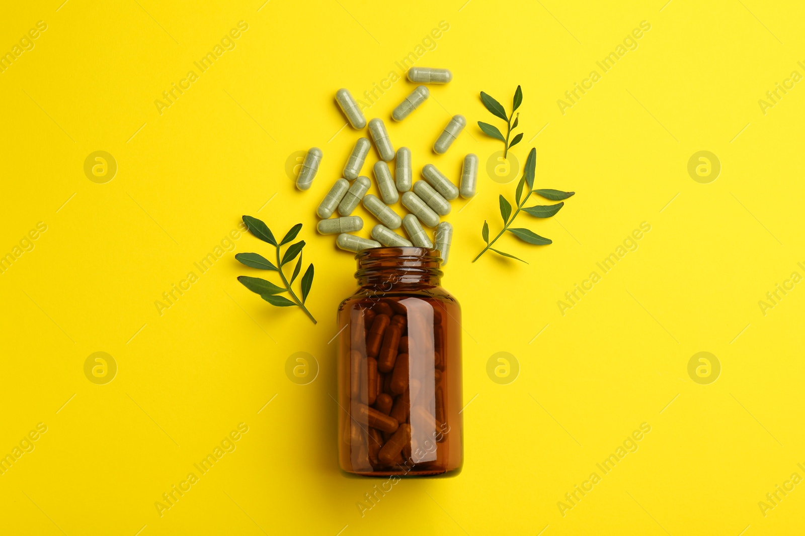 Photo of Vitamin pills, branches and bottle on yellow background, flat lay