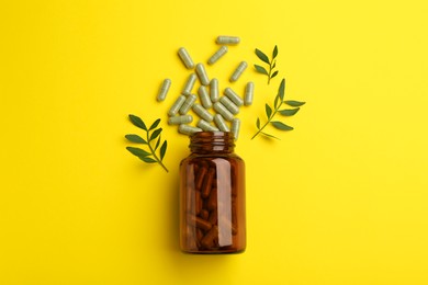 Vitamin pills, branches and bottle on yellow background, flat lay