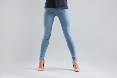 Photo of Woman wearing stylish jeans and high heels shoes on light gray background, closeup