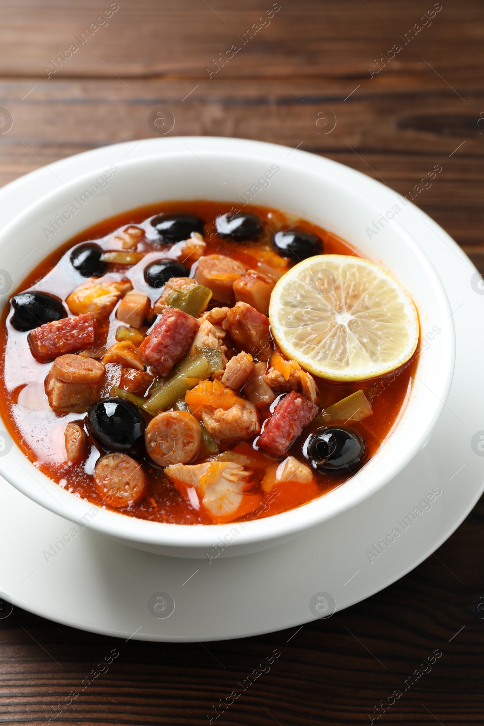 Photo of Meat solyanka soup with sausages, olives and vegetables on wooden table