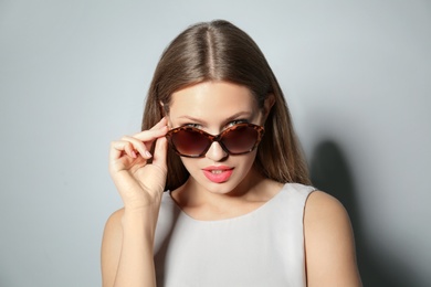 Photo of Young woman wearing stylish sunglasses on light grey background