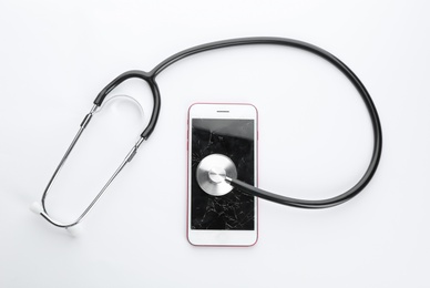 Photo of Modern smartphone with broken display and stethoscope on white background, top view. Device repair service