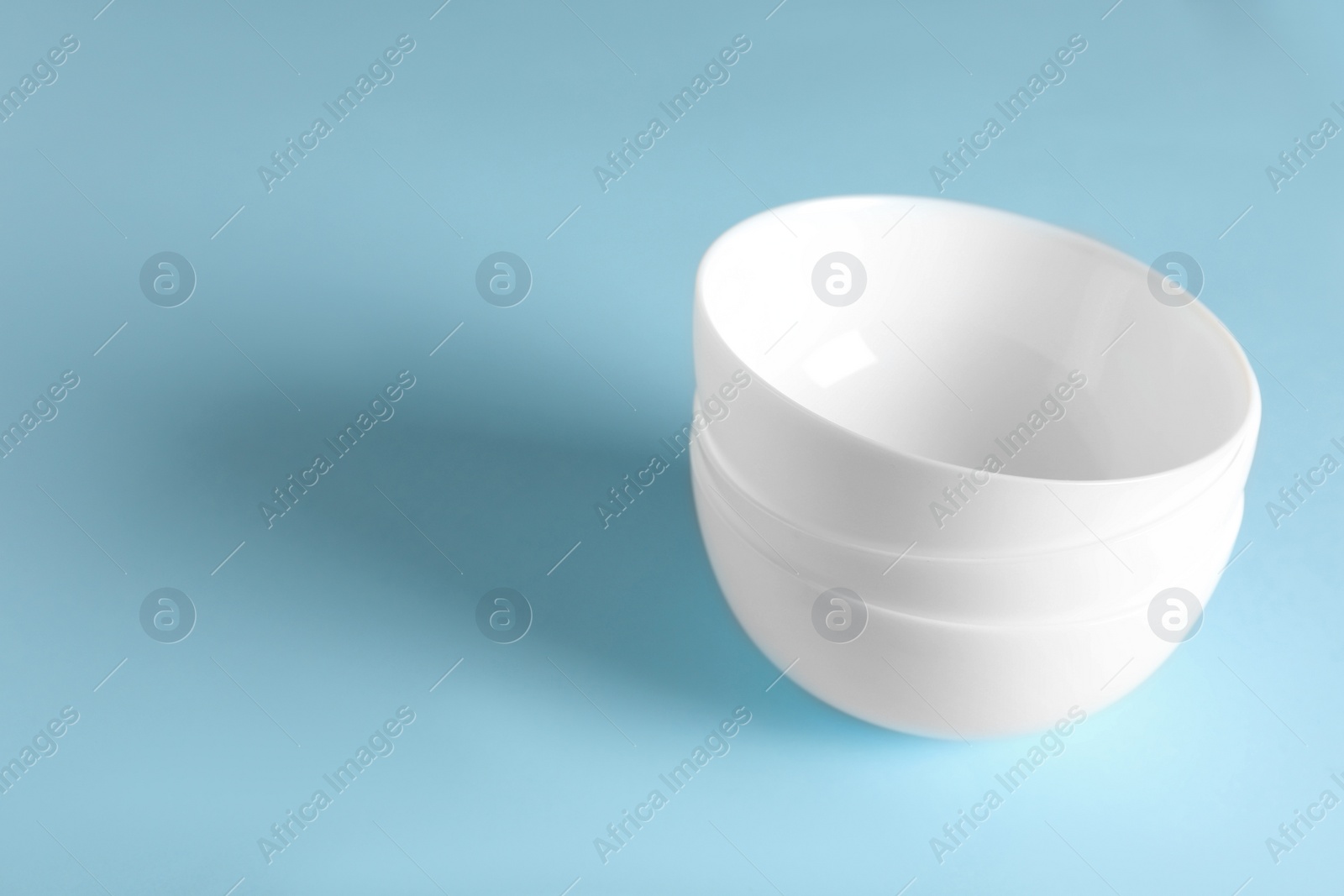 Photo of Empty ceramic bowls on light blue background. Space for text