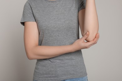 Photo of Woman suffering from pain in her elbow on light grey background, closeup. Arthritis symptoms