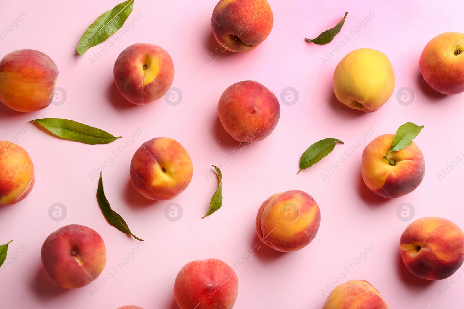 Photo of Fresh ripe peaches and green leaves on pink background, flat lay