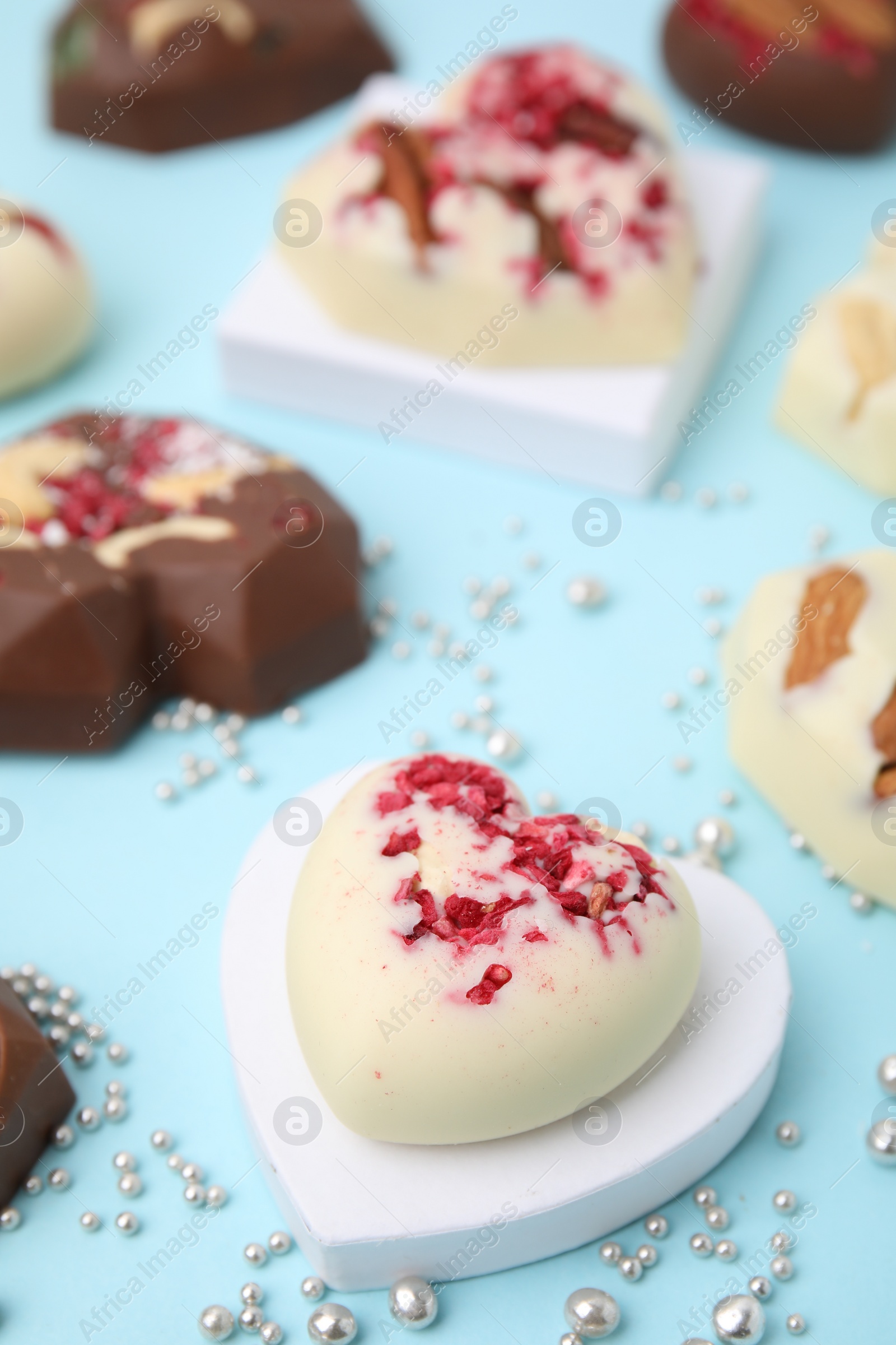 Photo of Tasty chocolate heart shaped candies with nuts on light blue background