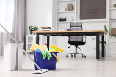 Photo of Cleaning service. Mop and bucket with supplies in office, space for text